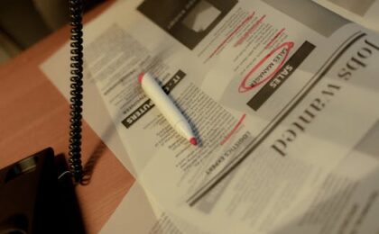Close-up of a newspaper job section with a red marker and corded phone on a table.